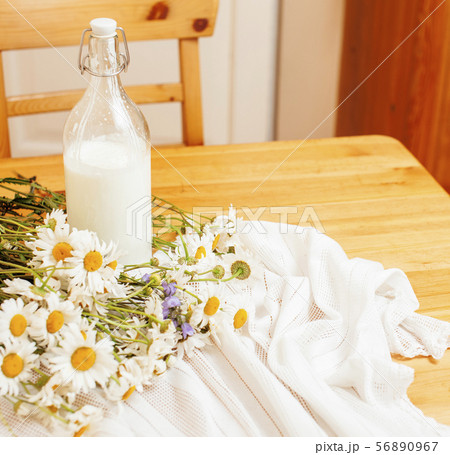 Simply stylish wooden kitchen with bottle of milk and glass on table, summer flowers camomile 56890967