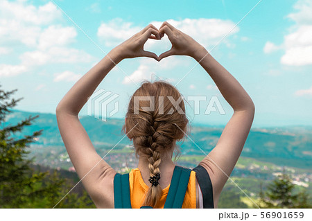 Woman hand forms a love hand with a blurred background of mountain and sky 56901659
