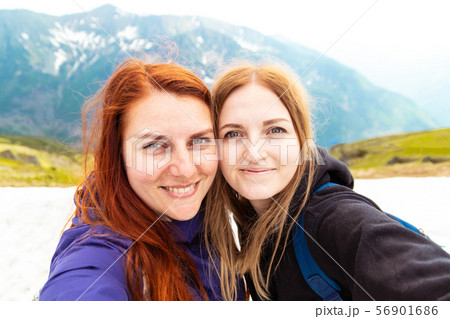 Two girls take a picture with their mobile. Two friends enjoy nature and the outdoors. 56901686