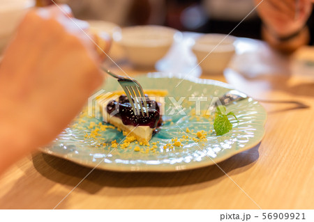 Woman hands with fork eating blueberry cheese cake in restaurant. Woman hands with fork eating blueberry cheese cake in restaurant. 56909921