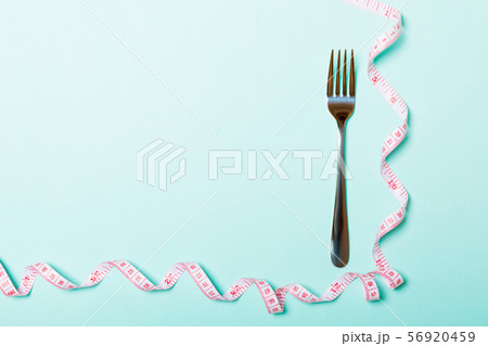 Fork with curled measuring tape on blue background Fork with curled measuring tape on blue background 56920459