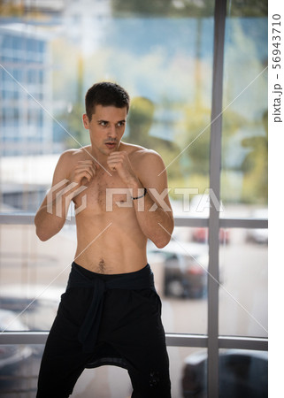An athletic man standing in fighting pose in the studio with glass windows 56943710