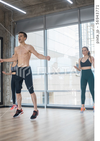 Fitness training in the bright studio - two young women training with their coach - jumping 56943771