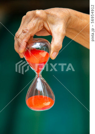 Senior woman's right hand holding red hourglass in blue swimming pool background, Close up & Macro shot, Selective focus, Time concept Senior woman's right hand holding red hourglass in blue swimming pool background, Close up & Macro shot, Selective focus, Time concept 56954912
