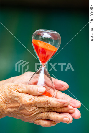 Senior woman's hands holding red hourglass in blue swimming pool background, Close up & Macro shot, Selective focus, Time concept 56955087