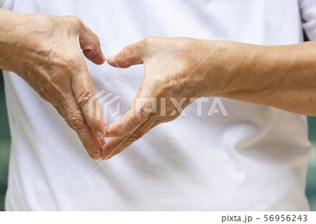 Senior woman's hand shaping of heart symbol on white t-shirt background, Body language concept Senior woman's hand shaping of heart symbol on white t-shirt background, Body language concept 56956243
