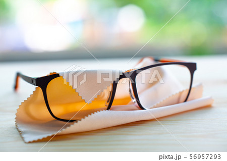 Black eyeglasses with ivory colour Microfibre cleaning cloths on wooden table, In bokeh green garden background, Close up & Macro shot, Selective focus, Optical concept Black eyeglasses with ivory colour Microfibre cleaning cloths on wooden table, In bokeh green garden background, Close up & Macro shot, Selective focus, Optical concept 56957293