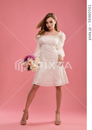 Brunette in a summer dress on a pink isolated background with a bouquet of flowers in her hands. 56960501