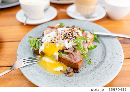 Breakfast and coffee in the summer cafe. Sandwich on a bun brioche with bacon, mushrooms, arugula Breakfast and coffee in the summer cafe. Sandwich on a bun brioche with bacon, mushrooms, arugula 56970451