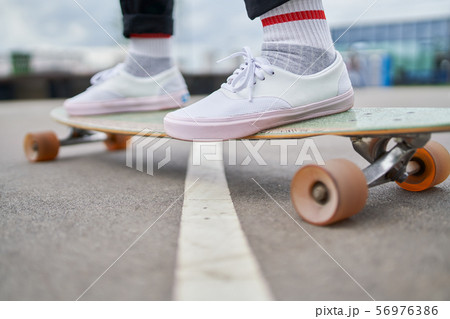 Photo of woman's legs in white sneakers riding skateboard on street in city 56976386