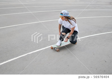 Photo on side of brunette woman in baseball cap riding skateboard outdoors 56976404