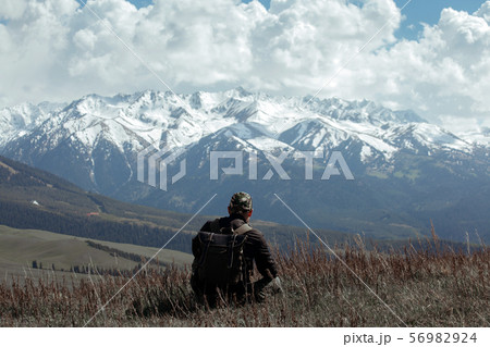 Man in camouflage sitting in dead grass in front of mountains 56982924