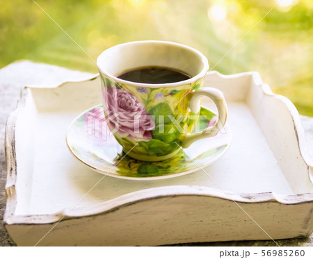 Hot morning coffee in small floral design cup on shabby chic vintage white tray on window sill in Hot morning coffee in small floral design cup on shabby chic vintage white tray on window sill in 56985260