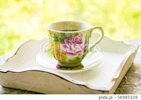 Hot morning coffee in small floral design cup on shabby chic vintage white tray on window sill in 56985328
