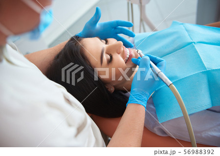 Male dentist in protective mask doing teeth cleaning for pretty lady 56988392
