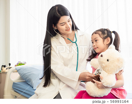 Beautiful doctor examination a little girl with used stethoscope to listening at the teddy bear for a child to relax. Beautiful doctor examination a little girl with used stethoscope to listening at the teddy bear for a child to relax. 56993164