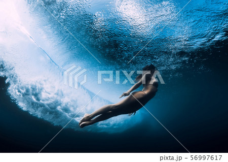 Woman in bikini dive without surfboard underwater with ocean wave. Duck dive under barrel wave 56997617