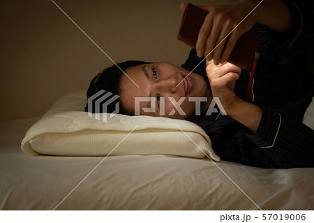 就寝前にスマホを見る日本人男性　ブルーライト　薄暗い 57019006