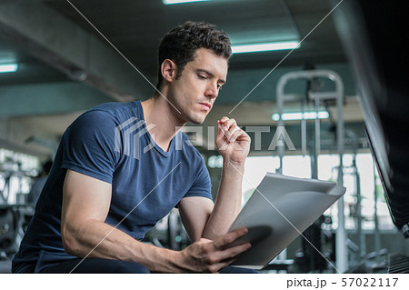Muscular handsome trainer looking at fitness plan Muscular handsome trainer looking at fitness plan 57022117