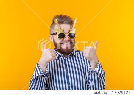 Joyful hipster young man raising his thumbs up in glasses with guitars posing against a yellow 57029128