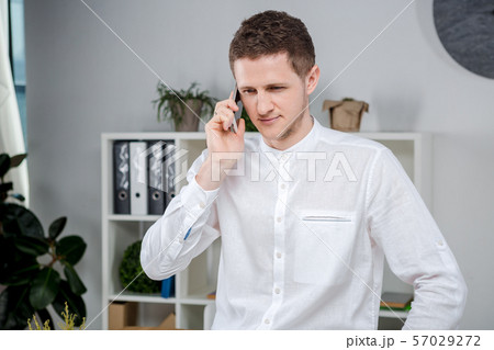 Attractive young businessman using a cell phone. Cheerful Businessman With Smartphone Standing In An Attractive young businessman using a cell phone. Cheerful Businessman With Smartphone Standing In An 57029272