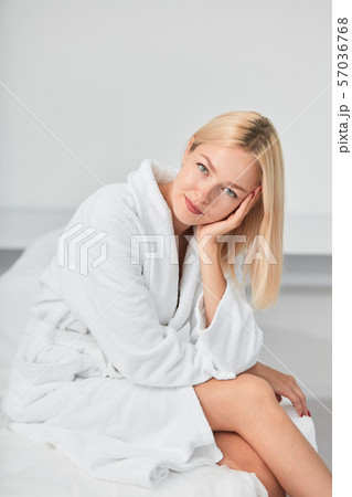 young awesome smiling woman in white bathrobe sitting in spa center on couch 57036768