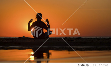 Young woman sits by the sea in lotus position at sunset, meditates 57037898