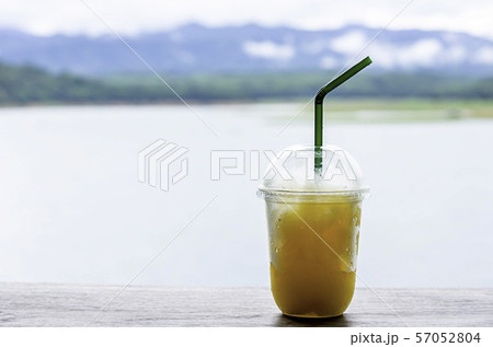 Glass of cold Orange juice smoothie on the table Background blurry views sky water and mountain. 57052804