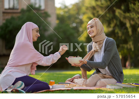 Friend wearing hijab sharing some blueberries with friend Friend wearing hijab sharing some blueberries with friend 57055654