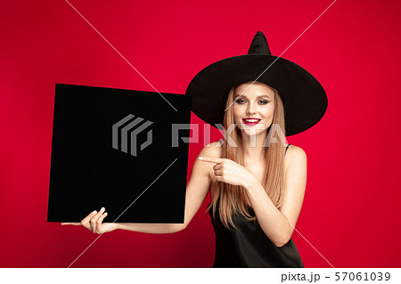 Young woman in hat as a witch on red background 57061039