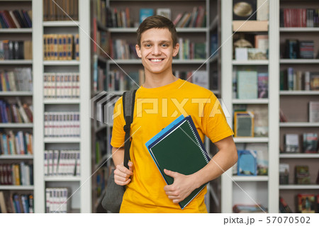 Handsome young guy standing in library, bookshelves background Handsome young guy standing in library, bookshelves background 57070502