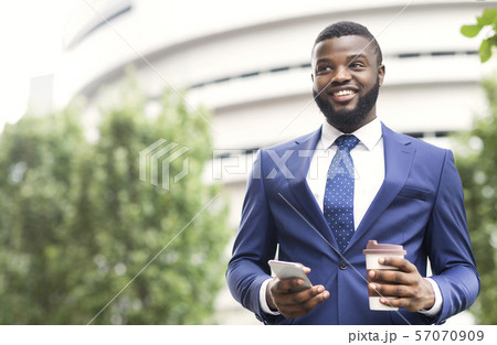 Handsome businessman standing outdoors with coffee and smartphone in arms 57070909