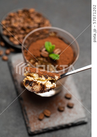 Portion of Classic tiramisu dessert in a glass cup on dark concrete background Portion of Classic tiramisu dessert in a glass cup on dark concrete background 57071202