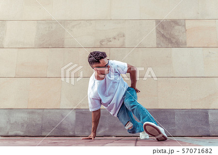 athlete man dancer in a white T-shirt, jeans glasses, dancing, summer in the city, background wall 57071682
