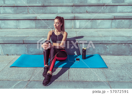 beautiful girl sits mat, fitness summer city, outdoors, yoga after workout, relaxation, enjoyment of 57072591