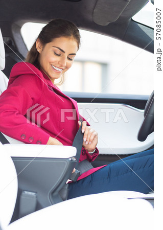 Businesswoman wearing bright jacket smiling while fastening seat belt Businesswoman wearing bright jacket smiling while fastening seat belt 57085007