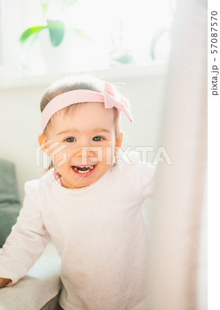 Caucasian baby girl in bright room, natural light. Looking into camera and laughing. 57087570