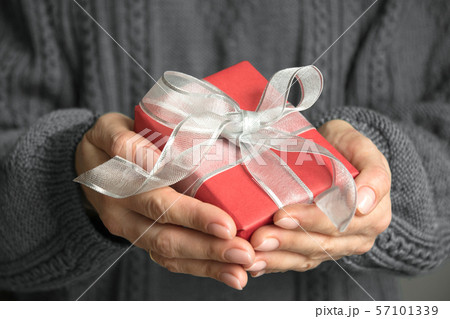 Female hands holding red gift wrapped with bow 57101339