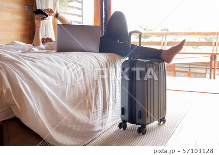 Relaxed businessman lying in bed looking at cellphone with laptop on his lap. Relaxed businessman lying in bed looking at cellphone with laptop on his lap. 57103128