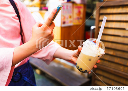 [原宿文化イメージ] 流行に敏感な少女がタピオカミルクティーを買ってスマホでSNSに投稿するシーン 57103605