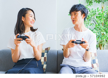 新婚夫婦のイメージ 仲睦まじく並んでテレビゲームを一緒に楽しむ若い男女 夫婦 恋人 カップルの写真素材