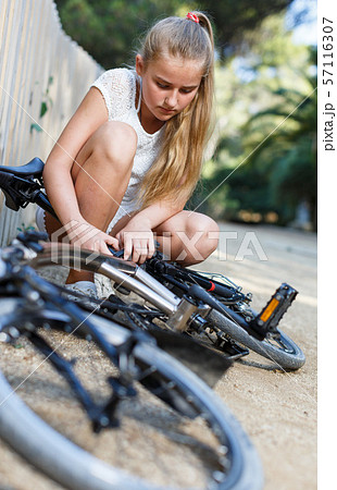 Teen girl girl checking bicycle near fence before ride in park Teen girl girl checking bicycle near fence before ride in park 57116307