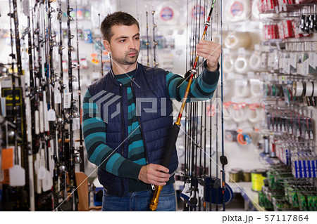 Young male shopper choosing ocean fishing rod Young male shopper choosing ocean fishing rod 57117864