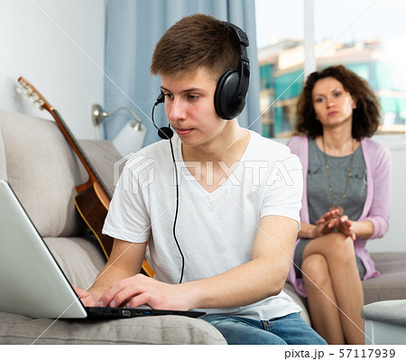 Teenager playing on laptop on background of worried mother Teenager playing on laptop on background of worried mother 57117939