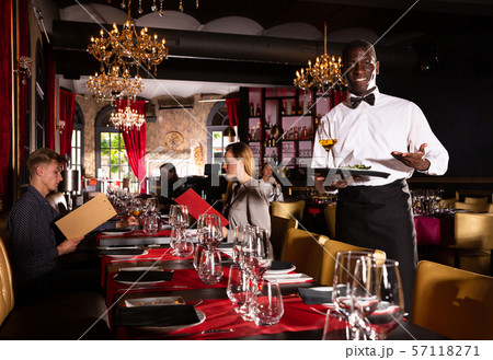 Hospitable african-american waiter standing with serving tray meeting restaurant guests Hospitable african-american waiter standing with serving tray meeting restaurant guests 57118271