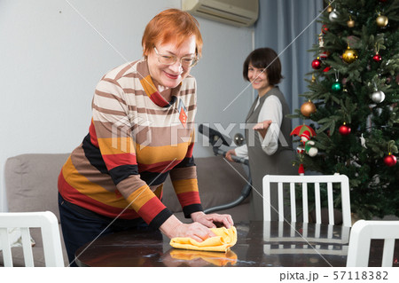 Mature woman wiping table, daughter vacuum cleaning sofa Mature woman wiping table, daughter vacuum cleaning sofa 57118382