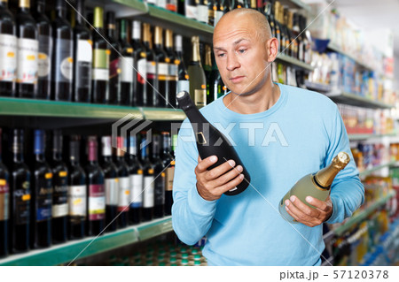 Serious male customer looking bottle wine in store indoor Serious male customer looking bottle wine in store indoor 57120378