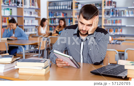 Portrait of upset tired male student preparing for exam in university library 57120705