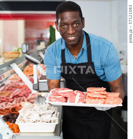 African American seller preparing fresh meat of lamb for sale in butcher store 57121063