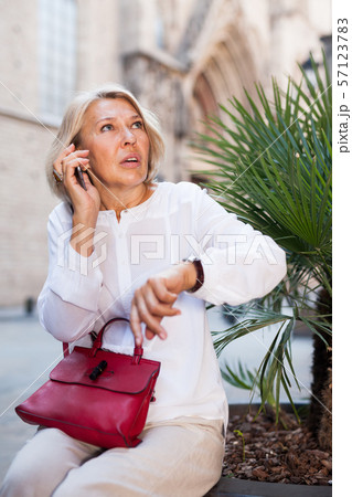 Hurrying woman looks at her watch and talking on the phone 57123783